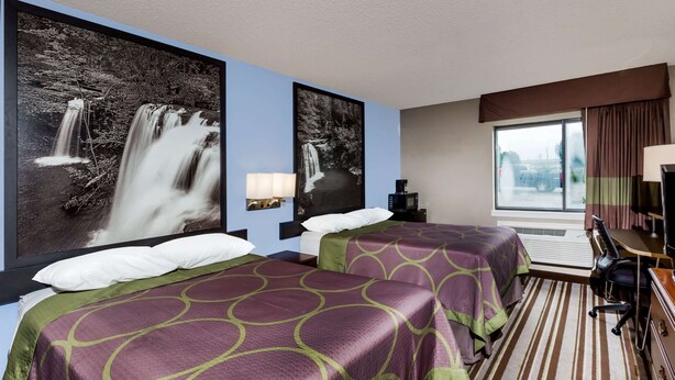 A hotel room with two beds, a desk, a chair, a lamp, and large waterfall artwork on the walls.