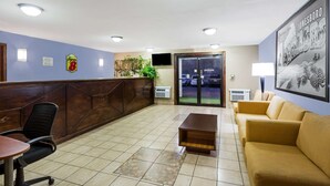 A reception area with a wooden reception desk, a black office chair, a beige sofa, a wooden coffee table, and a large framed picture on the wall.