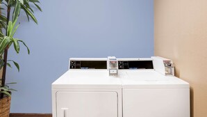 A front-loading washer and dryer unit with control panels, positioned against a blue and beige wall.
