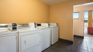 A laundry area with three stacked washers and dryers, a control panel, and a view of the outside through a glass door. - FairBridge Inn Express Stuttgart (Stuttgart)