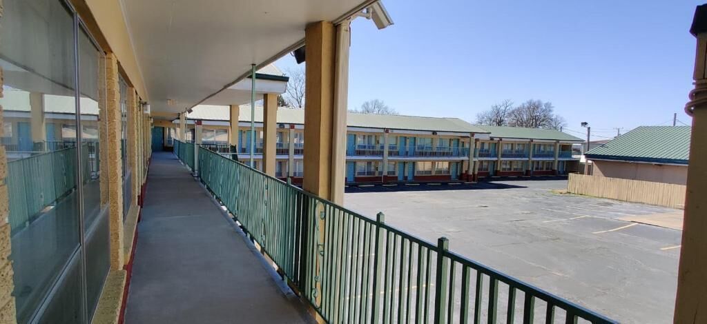 A long corridor with a covered walkway, leading to a parking area and a motel building with multiple floors.
