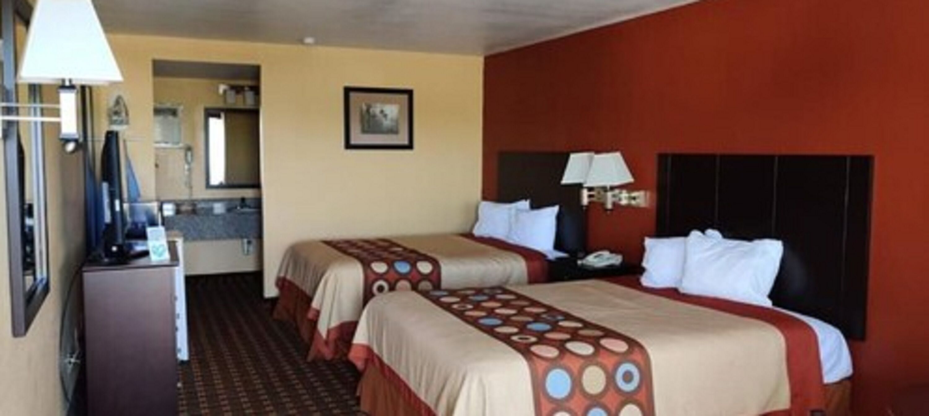 A hotel room with two beds, a desk, a lamp, and a picture on the wall.