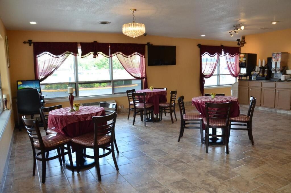 Un espace repas avec des tables et des chaises rondes, un lustre et une vue dégagée sur l’extérieur grâce à de grandes fenêtres.