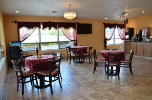 Un comedor con mesas y sillas redondas, una araña y vistas amplias a través de grandes ventanales.