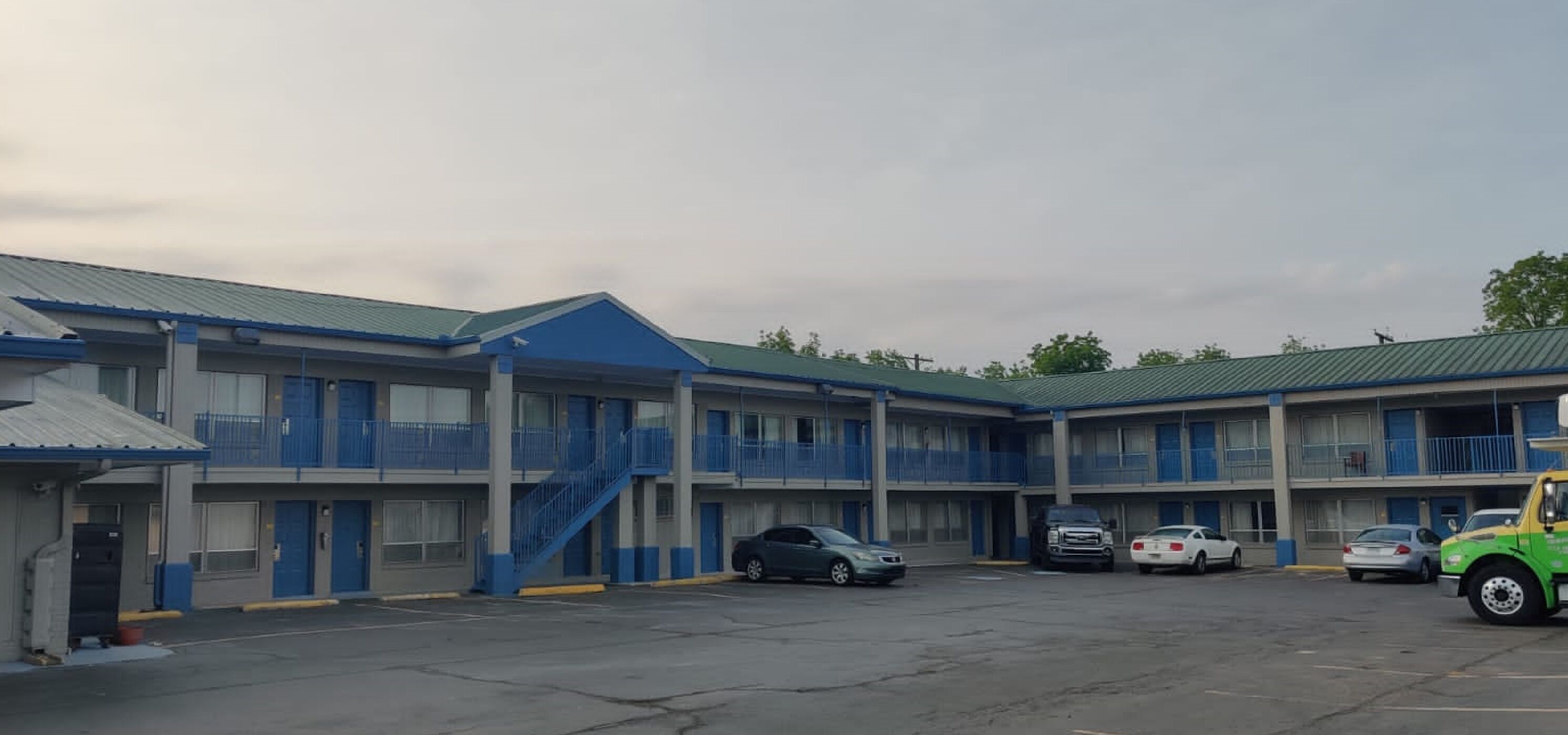 A motel with multiple floors, blue balconies, and a parking lot with several cars.