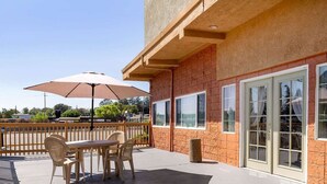 An outdoor patio with a table and chairs, a large umbrella, and a view of the street. - Auburn House Hotel (Auburn)