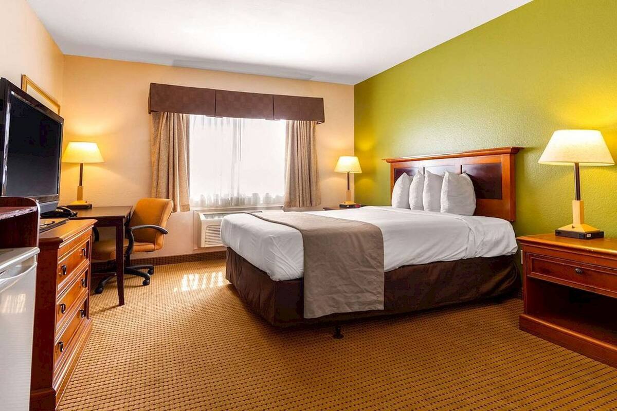 Ein Hotelzimmer mit Bett, zwei Nachttischlampen, einem Schreibtisch mit Stuhl, einem Fernseher und einem Fenster mit Vorhängen.