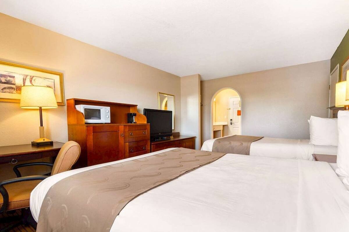 Ein Hotelzimmer mit zwei Betten, einem Schreibtisch mit Computer, einem Fernseher und einer Mikrowelle.