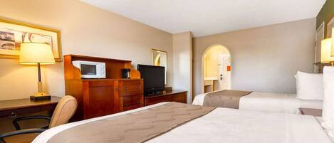 A hotel room with two beds, a desk with a computer, a TV, and a microwave.