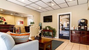 A living room with a sofa, coffee table, and a TV mounted on the wall. There is a door leading to a kitchen area with a coffee machine. - Auburn House Hotel (Auburn)