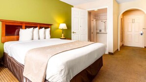 A hotel room with a large bed, a nightstand with a lamp, a shower area, and a door leading to another room. - Auburn House Hotel (Auburn)