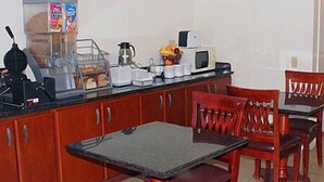 A compact kitchen with a dining area, equipped with a coffee maker, microwave, and a fruit bowl on the counter. - Motel 6 Fresno, CA (Fresno)