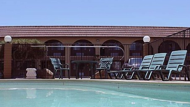 A pool area with lounge chairs and a building with arched windows in the background. - Motel 6 Fresno, CA (Fresno)