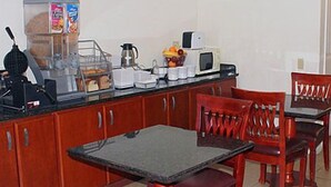 A kitchen with a dining table and chairs, a coffee maker, a microwave, and a fruit basket. - Motel 6 Fresno, CA (Fresno)
