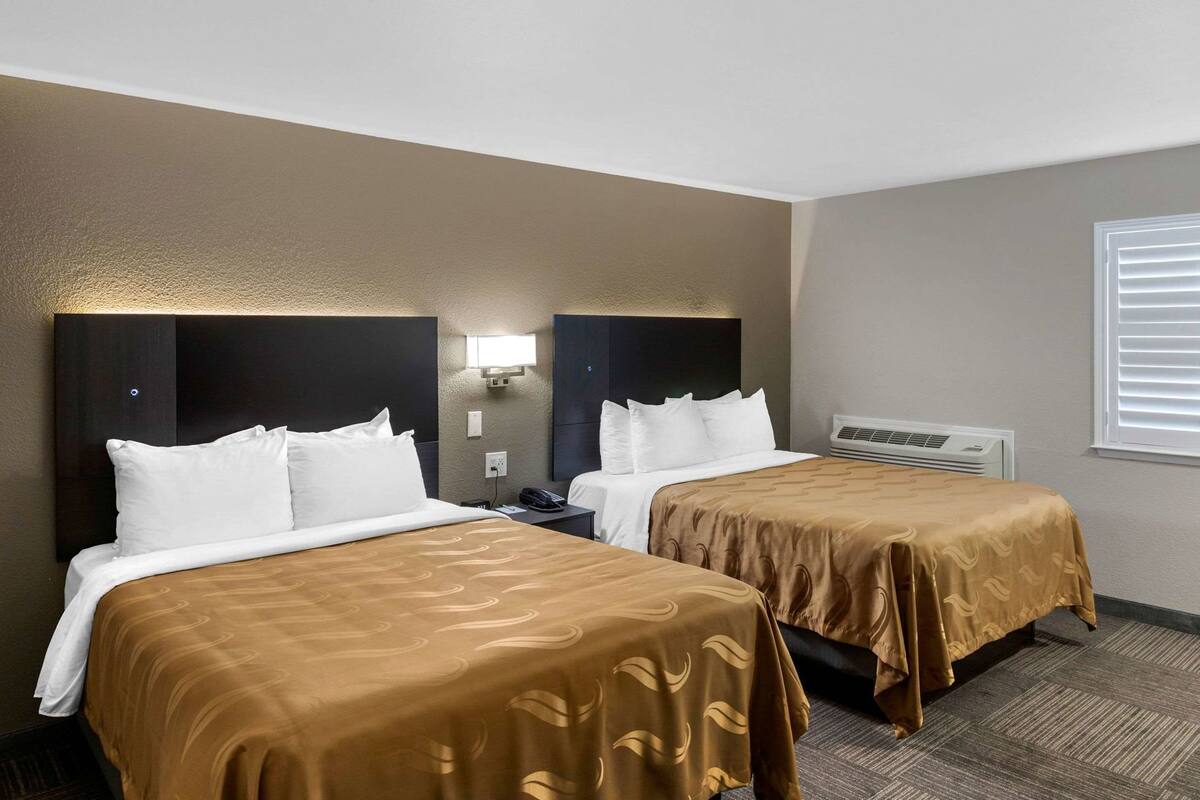 Ein Hotelzimmer mit zwei Betten, einem Nachttisch, einer Lampe und einem Fenster mit Jalousien.