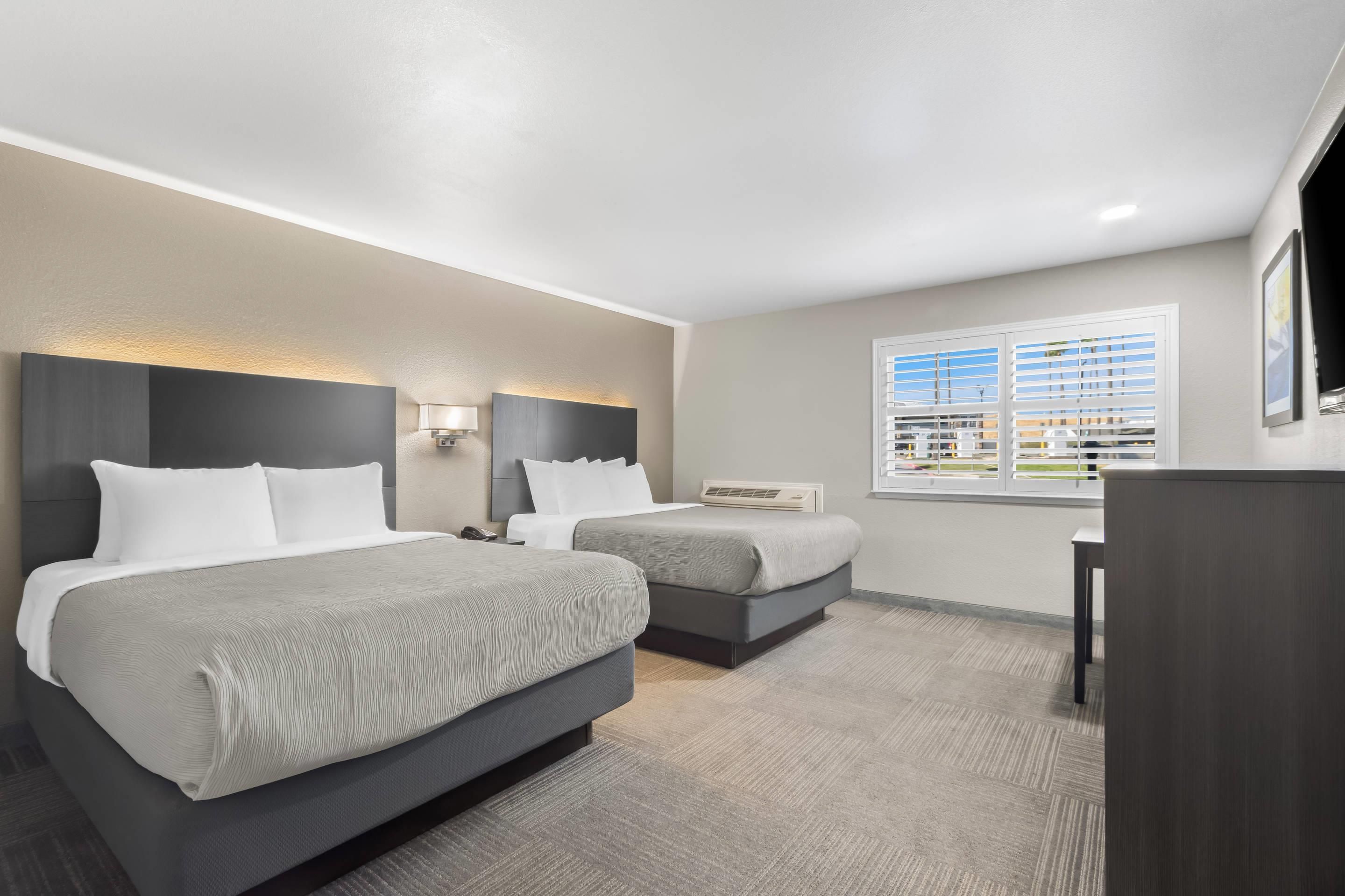 A hotel room with two beds, a desk, a chair, a TV, and a window with blinds.