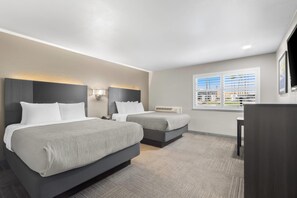 Een hotelkamer met twee bedden, een bureau, een stoel, een televisie en een raam met zonwering.
