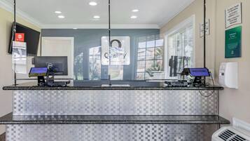 Zona de recepción con mostrador de check-in, dos monitores de ordenador, un cartel que dice “Calidad by Choice Hotels” y una ventana con vistas al exterior.
