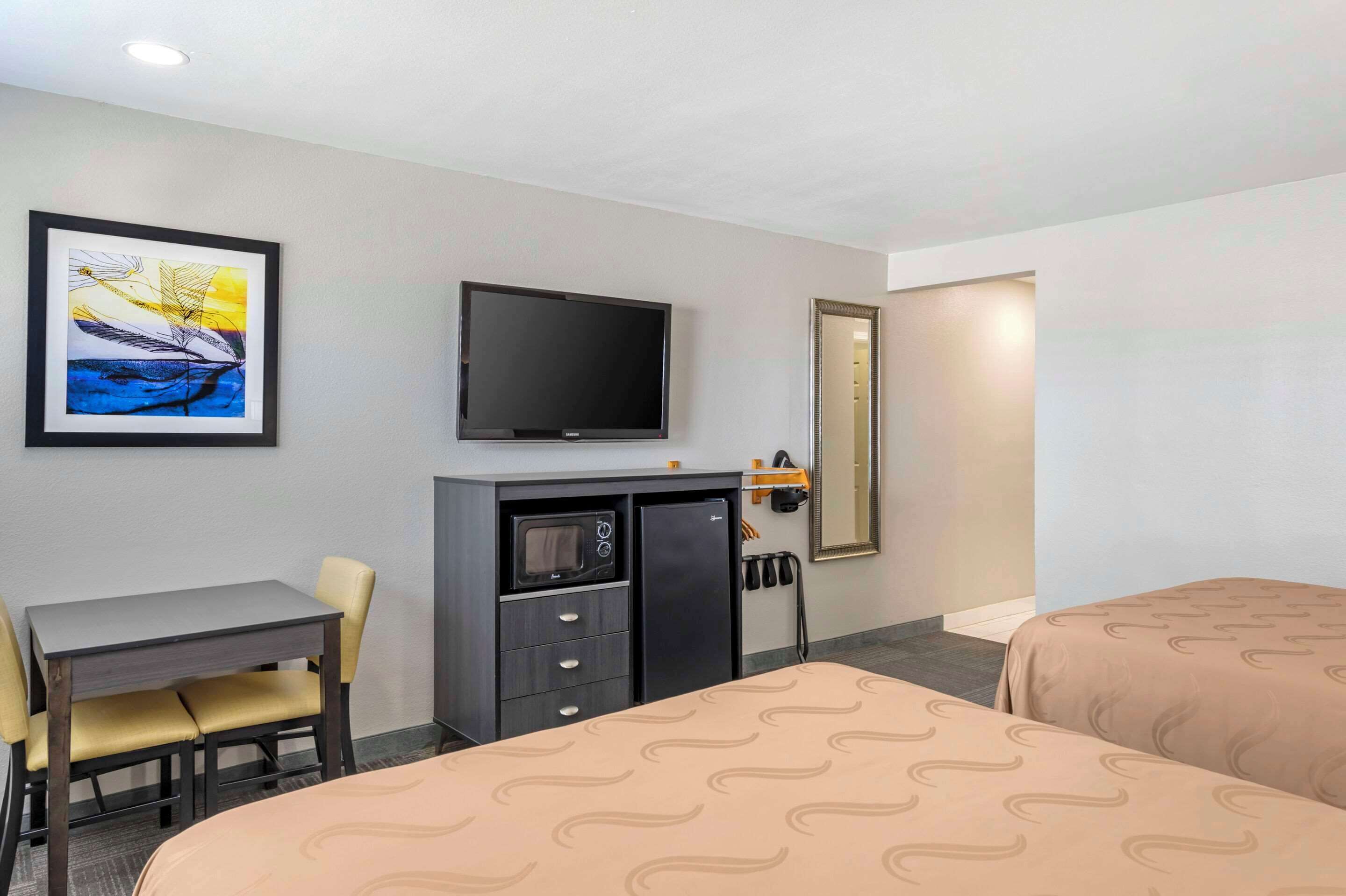 A hotel room with a bed, a desk with a chair, a television, a minibar, and a framed picture on the wall.