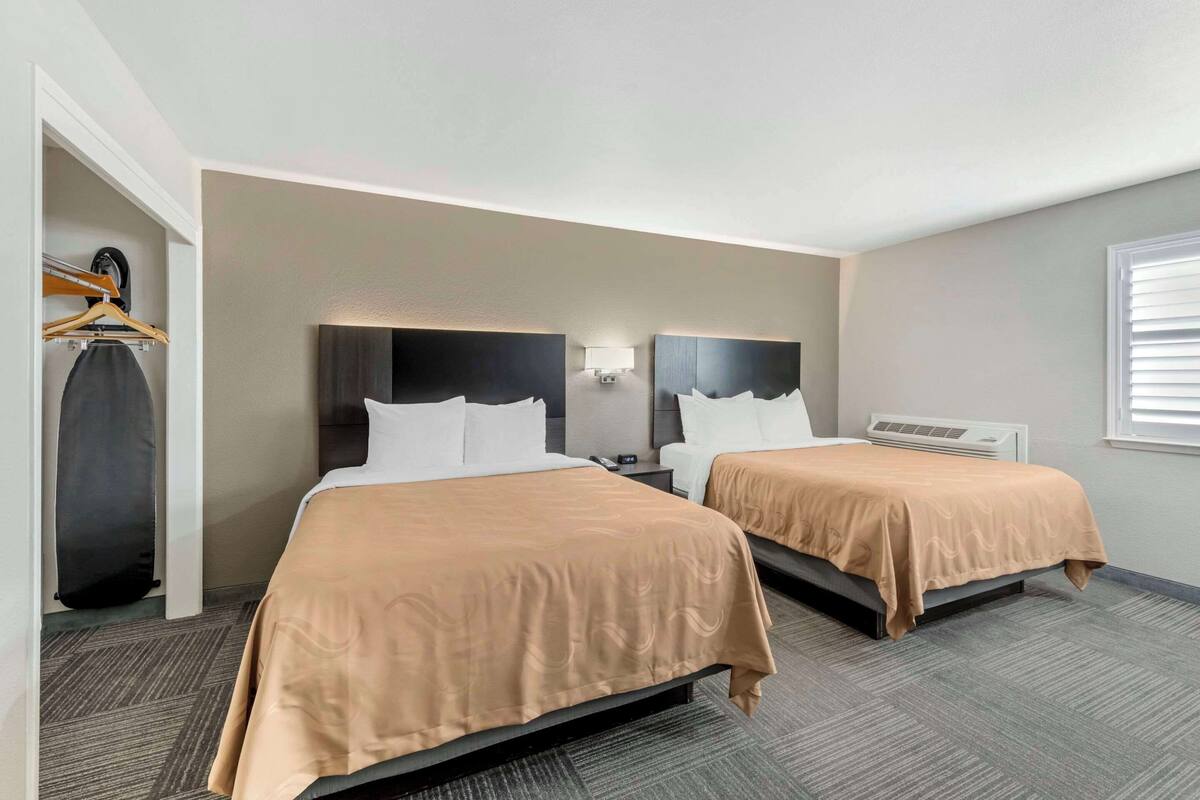 Ein Hotelzimmer mit zwei Betten, einem Schrank, einem Schreibtisch und einem Fenster.