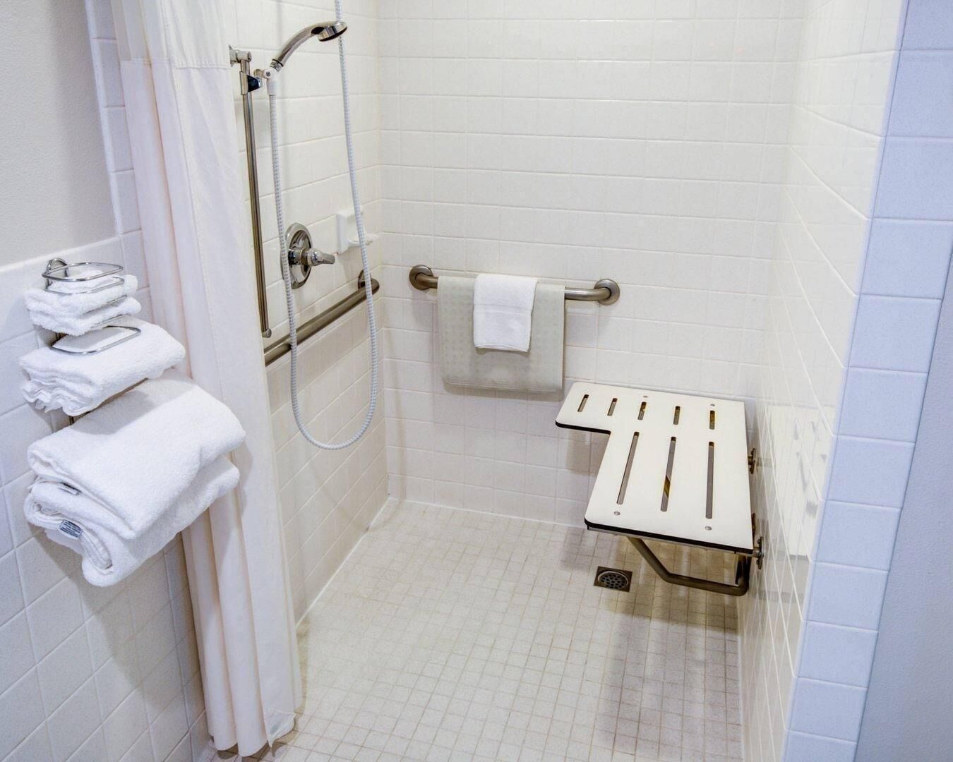 A shower with a handheld showerhead, a towel rack with folded towels, and a grab bar.