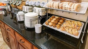 Una mesa de buffet con distintos alimentos, entre ellos pasteles y productos de repostería.