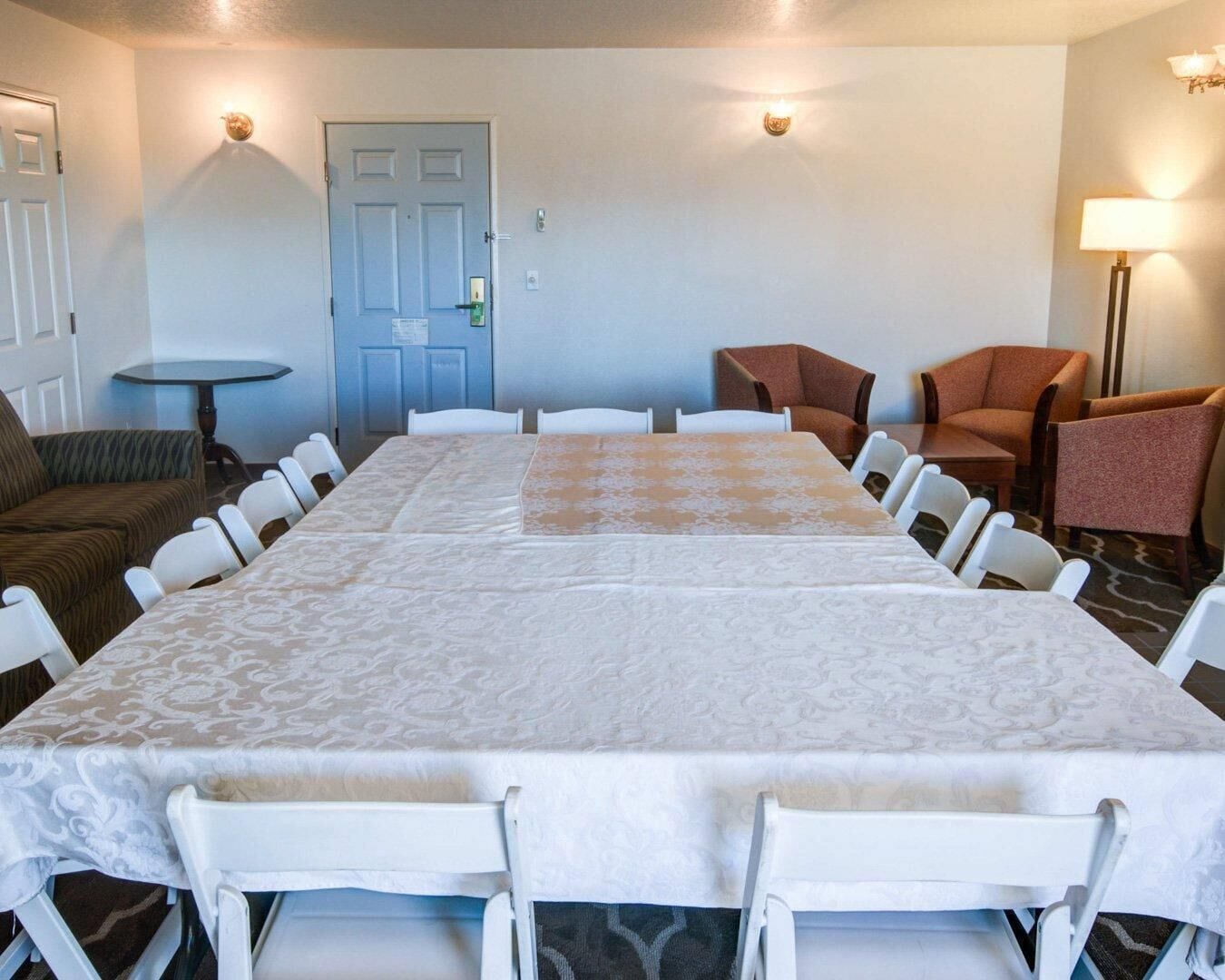 A conference room with a long table, white chairs, a sofa, and two lamps.