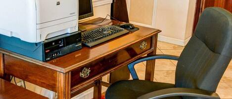 A wooden desk with a printer, a computer monitor, a keyboard, and a chair.