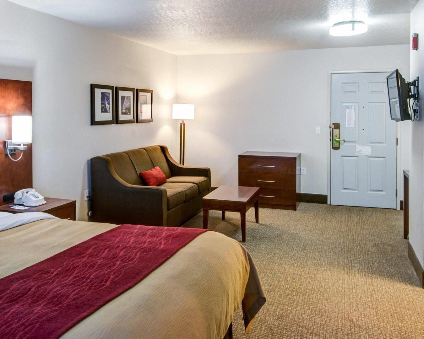 A hotel room with a bed, a sofa, a desk, a lamp, a TV, and a door.