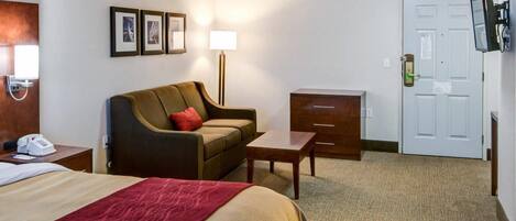 A hotel room with a bed, a sofa, a desk, a lamp, a TV, and a door.
