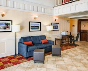 A hotel lobby with a blue sofa, two side tables, a desk with a chair, and a red and yellow patterned rug.