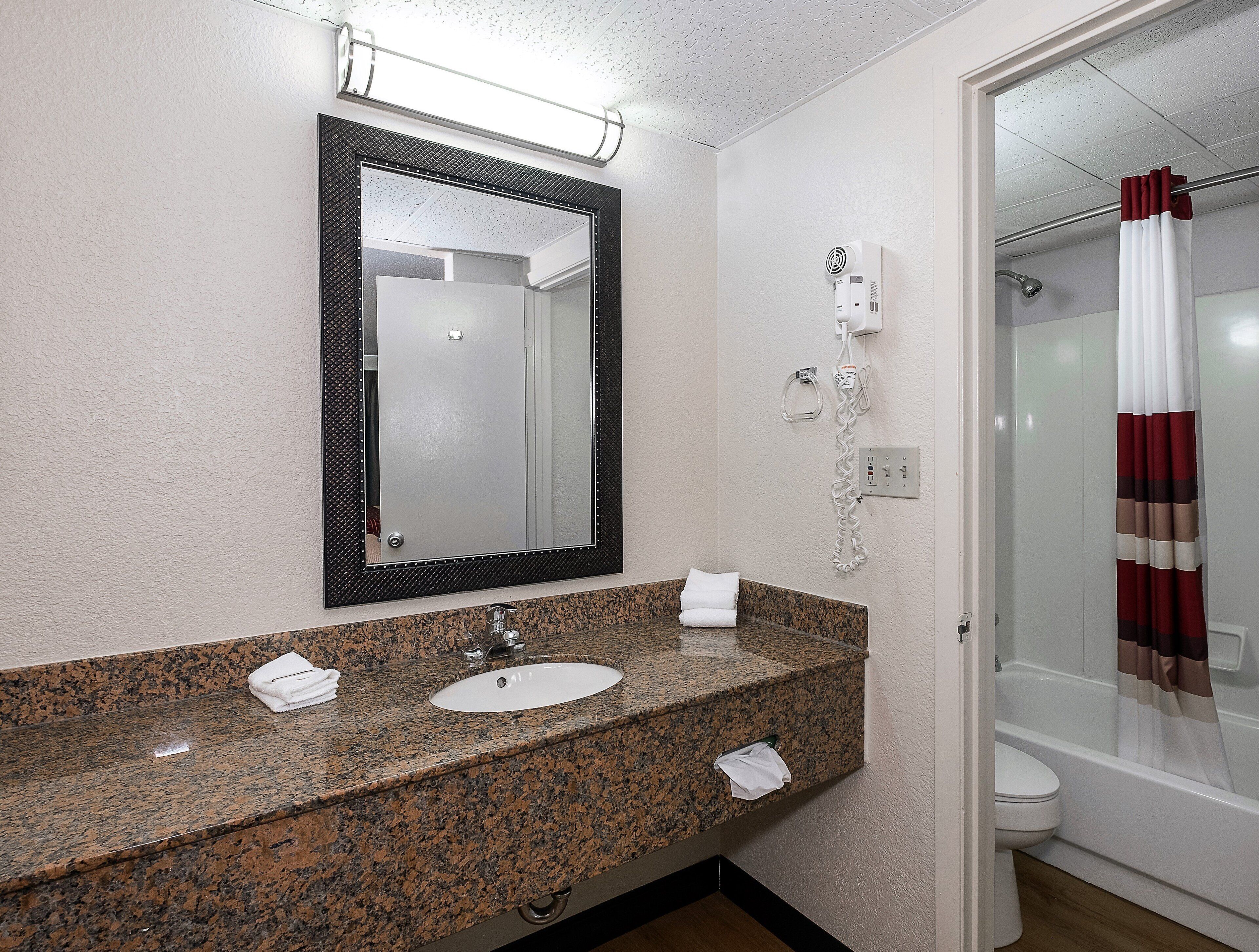 A bathroom with a granite countertop sink, a mirror, a handheld showerhead, and a toilet.