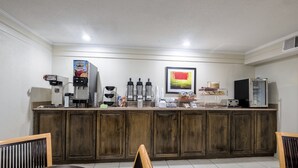A kitchen with a coffee machine, a refrigerator, and a dining area with a table and chairs. - Red Roof Inn Bloomington - Normal/ University (Bloomington)