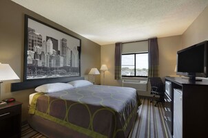 Una habitación de hotel con cama, escritorio, televisor y un amplio ventanal con cortinas.