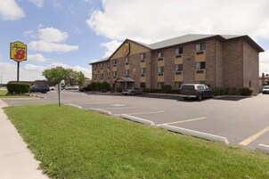 Un hotel Super 8 con fachada de ladrillo, múltiples ventanas y un estacionamiento con varios automóviles.