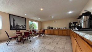 A spacious kitchen with a dining area, featuring a large window, a cityscape artwork, and stainless steel appliances.