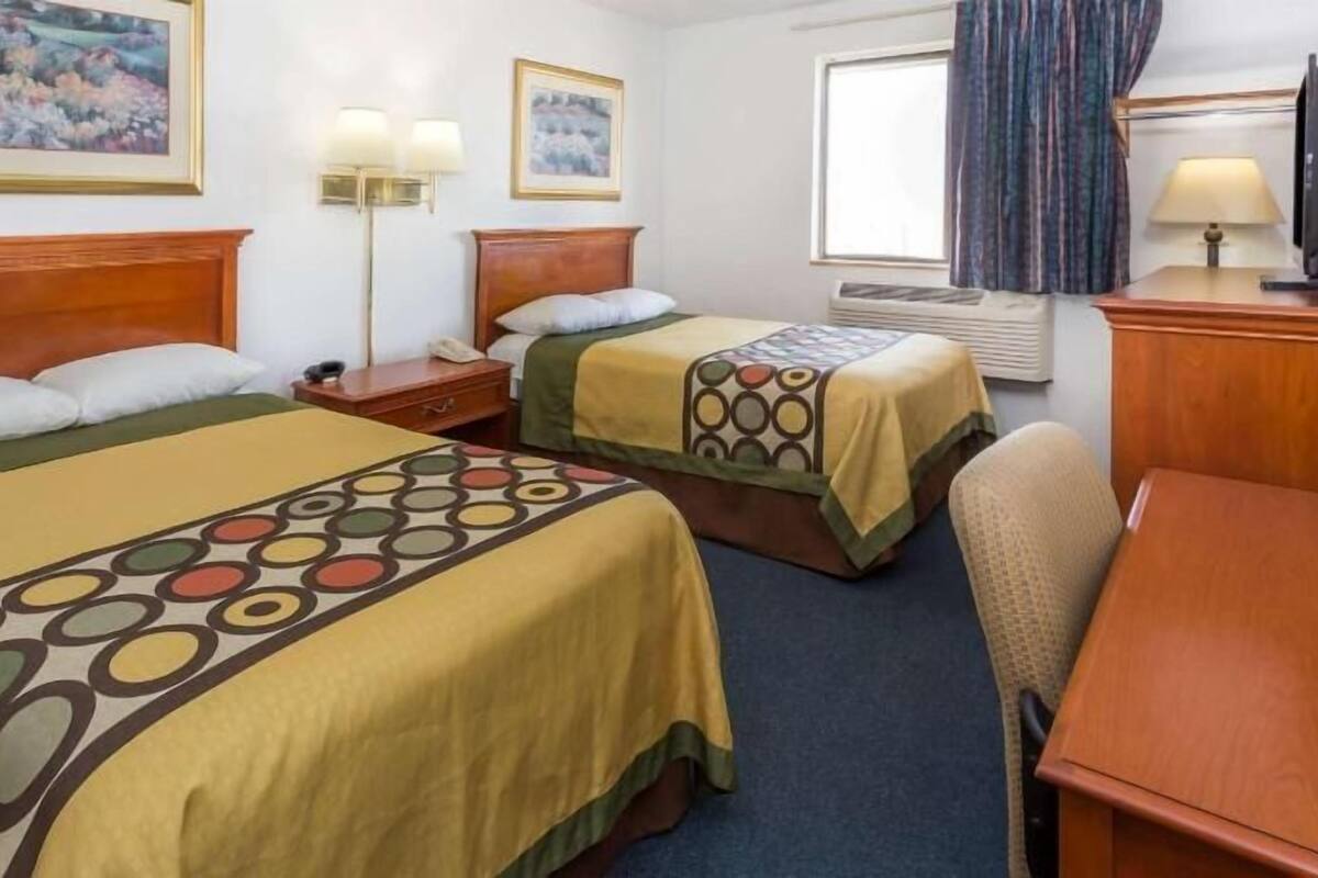 A hotel room with two beds, a desk, a chair, a TV, and artwork on the walls.