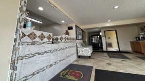 A hotel lobby with a reception desk, patterned tiles, a patterned armchair, and a doormat with a logo.