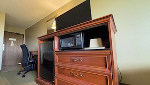 A wooden dresser with a microwave on top, drawers, and a flat-screen TV.