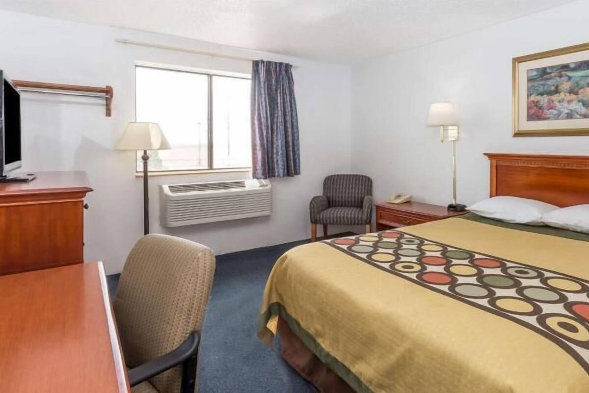 A hotel room with a bed, a desk, a chair, a TV, an air conditioner, and a painting on the wall.