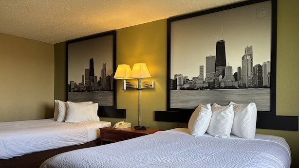A hotel room with two beds, a nightstand with a lamp, and two large cityscape paintings on the walls.