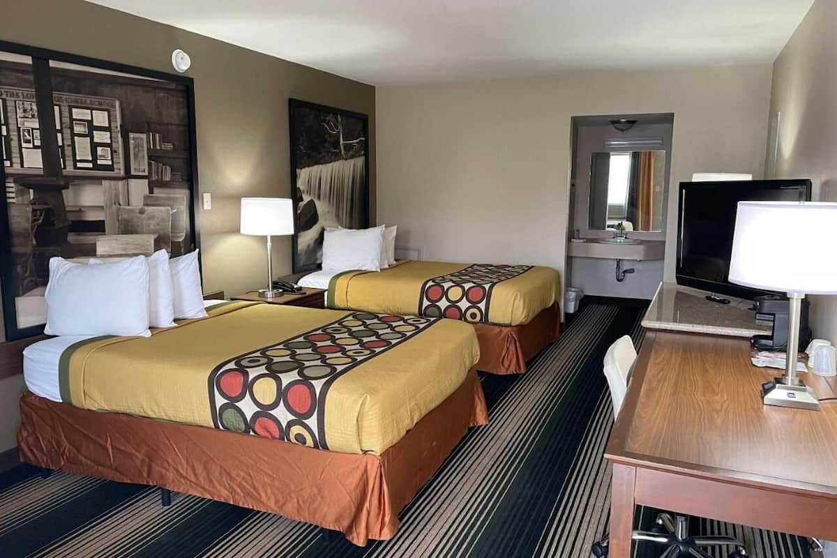 Ett hotellrum med två sängar, ett skrivbord, en stol, en tv och en spegel.