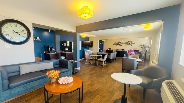 Een moderne woonkamer met een bank, salontafel en stoelen, een eethoek met tafels en stoelen, en een keuken met een televisie en aanrecht.