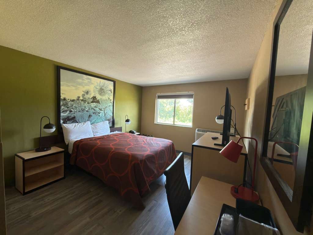 A bedroom with a bed, bedside table, desk, chair, and a window.