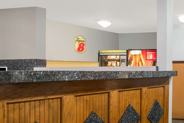Ein Hotel-Empfangsbereich mit einer Rezeption, einem Schild mit der Aufschrift "Super 8" und einer Vitrine mit Gegenständen.