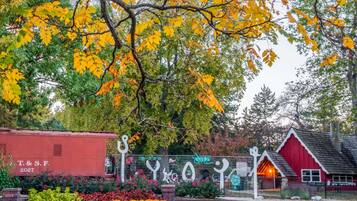 A red barn with a white door, surrounded by autumn foliage and a decorative fence.