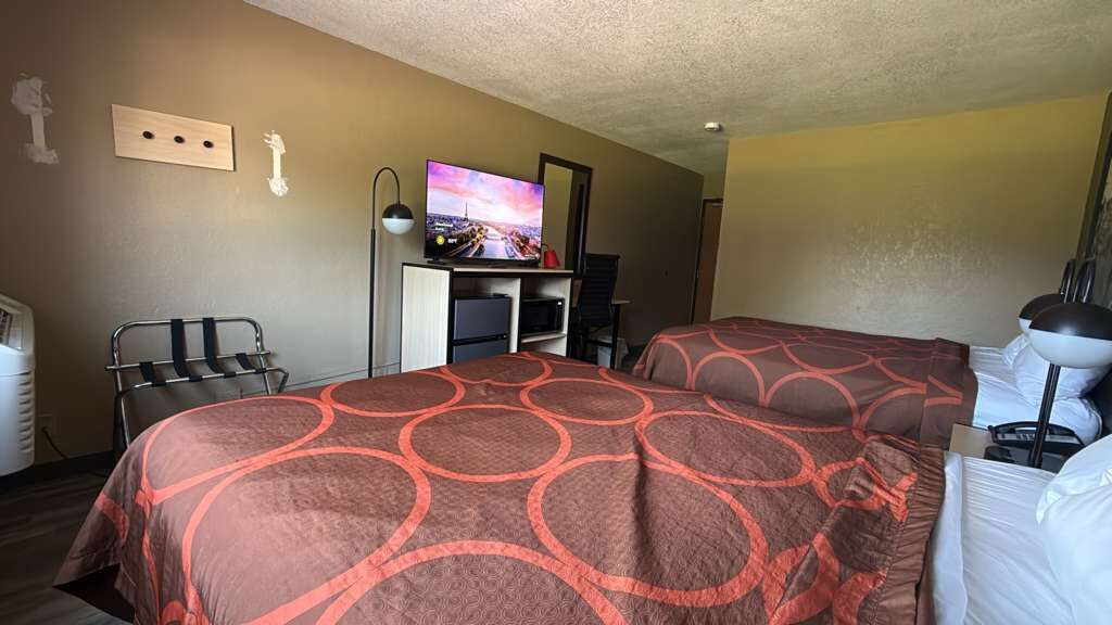 Habitación de hotel con dos camas, un televisor, un escritorio con computadora y una silla.