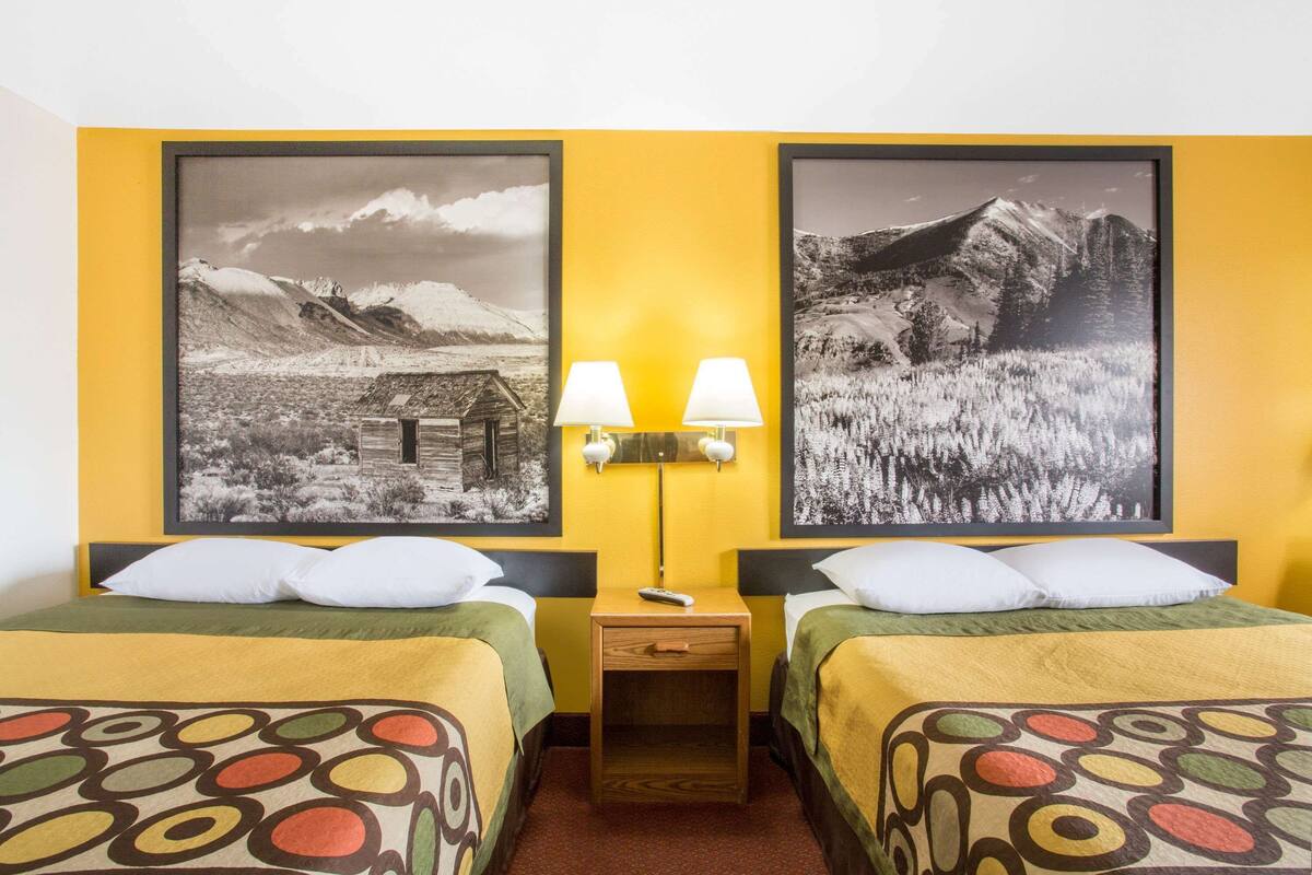 A hotel room with two beds, each with a colorful patterned bedspread, a nightstand with two lamps, and two framed black and white photographs on the wall.