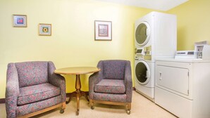 A room with two patterned armchairs, a small round table, and a front-loading washing machine. - Super 8 by Wyndham Elko (Elko)