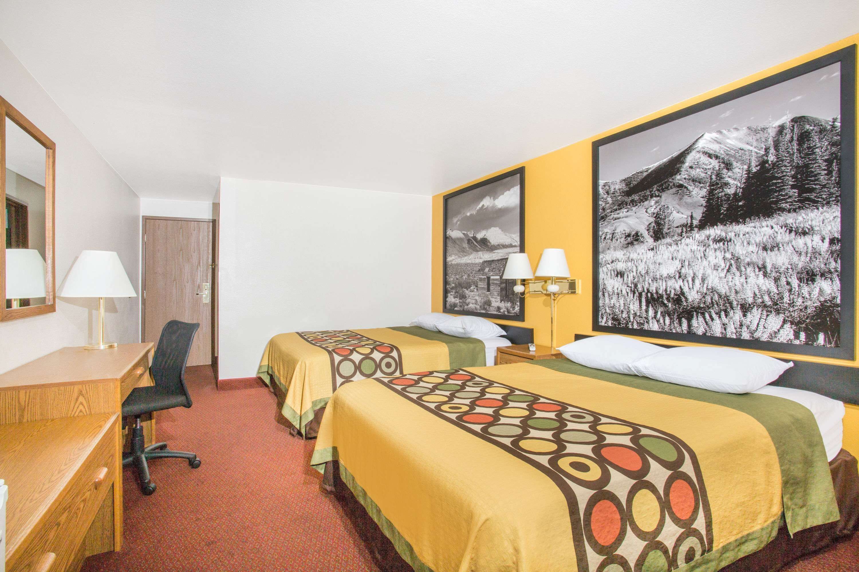 Habitación de hotel con dos camas individuales, un escritorio, una silla y un ventanal amplio.